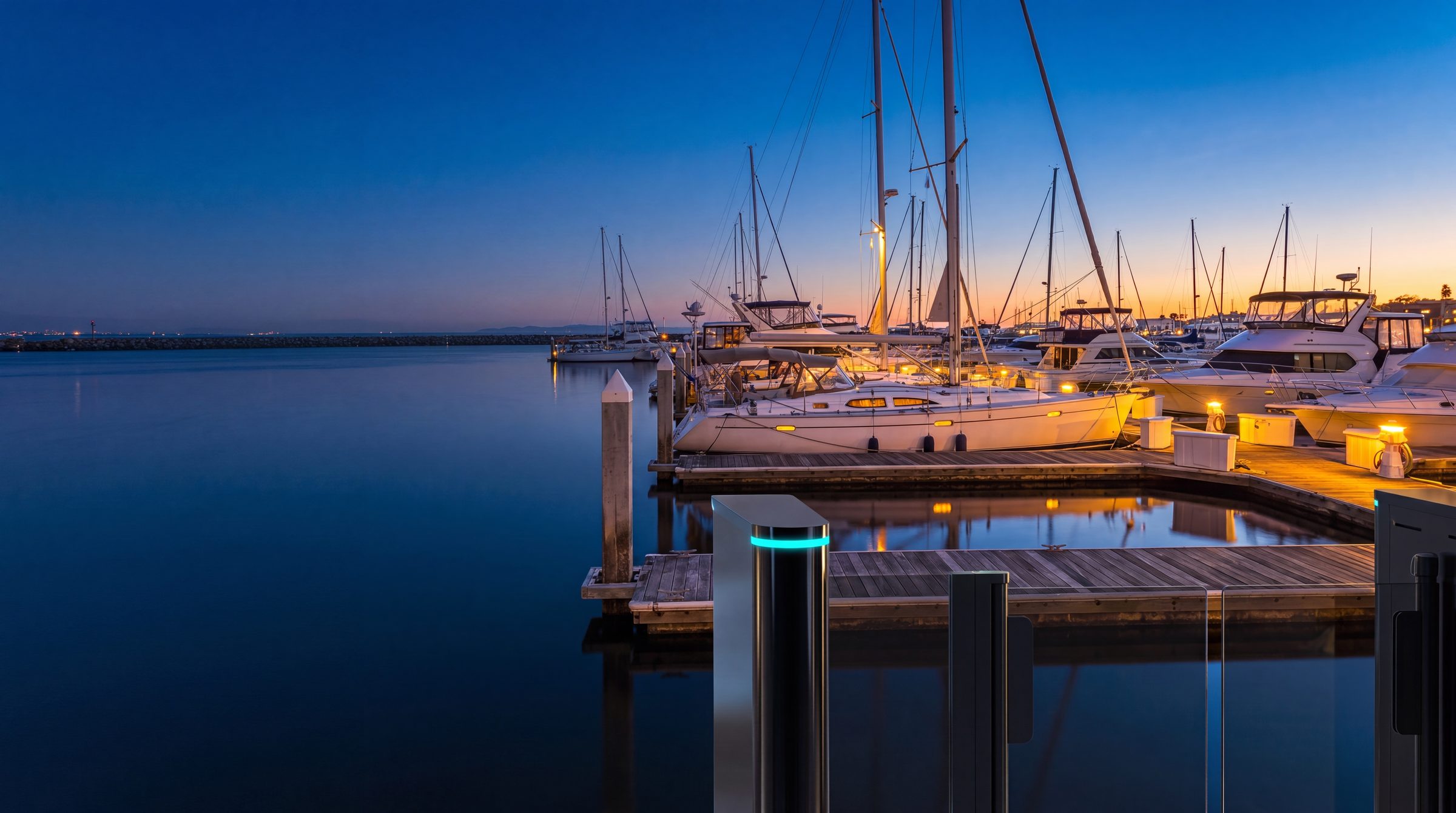 Blue-hour marina at dusk with a cyan-glowing access pedestal on the dock